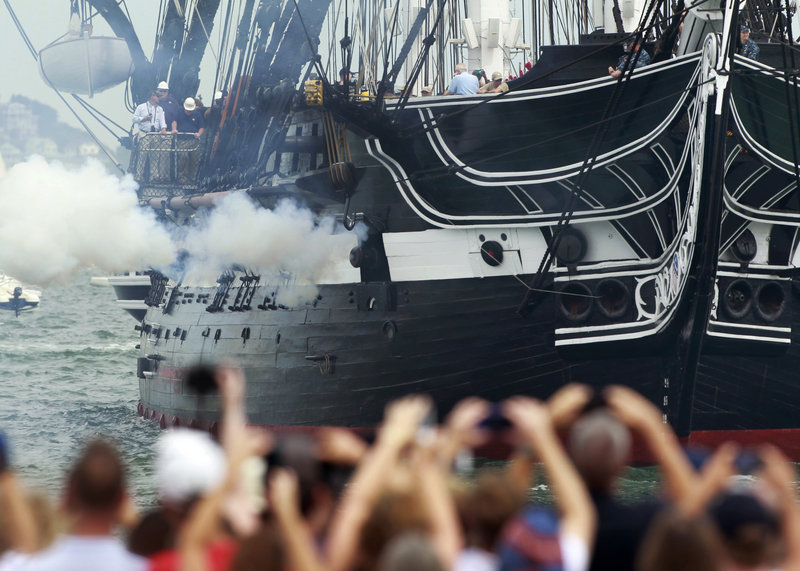 The USS Constitution fires one of its guns in Boston Harbor as a crowd looks on from the shore Sunday.