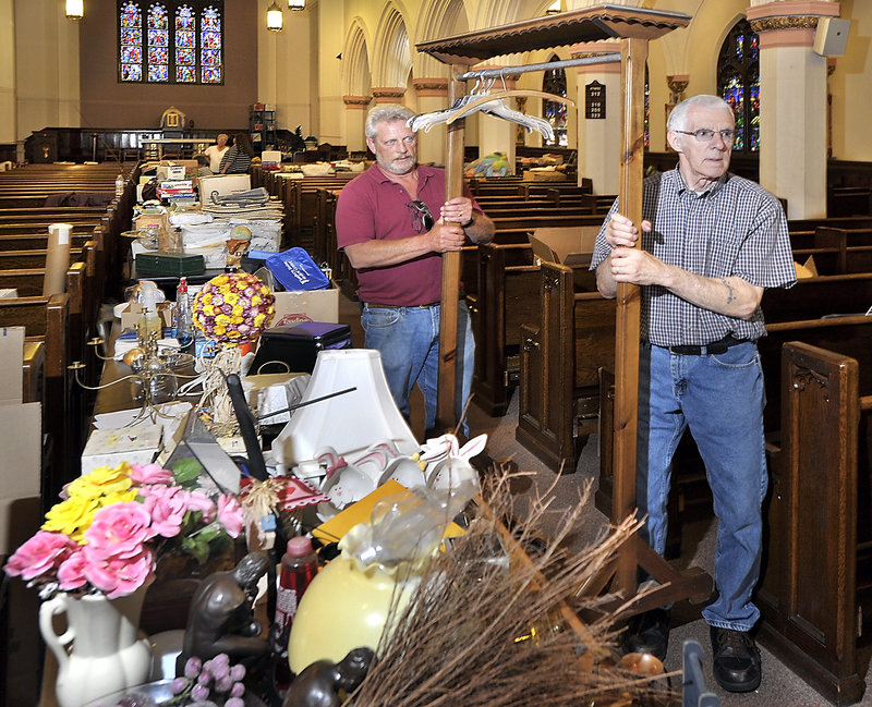 Robert Labelle, left, buildings project coordinator for Good Shepherd Parish, and volunteer Ben Forcier, move a coat rack past items that will be available at a yard sale Friday, Saturday and possible Sunday at the now closed St. Mary’s Church in Biddeford.