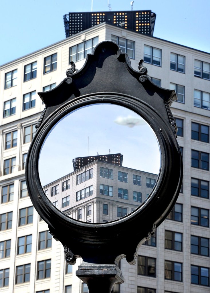 A clock in Portland’s Monument Square is covered by a painting that looks like a mirror reflecting the top of the Time and Temperature building, with a UFO hovering nearby.