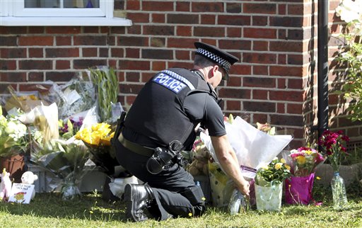 A police officer places flower tributes Saturday outside the Claygate, England, home of Saad al-Hilli, during investigations into the shooting deaths of al-Hilli, his wife and two other people Wednesday in the French Alps. The al-Hillis' 7-year-old daughter, Zaina, who was shot in the shoulder, came out of an induced coma Sunday but cannot yet talk to investigators. Her sister, Zeena, 4, escaped injury by hiding under her mother's skirt.