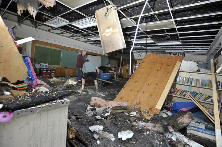 Volunteers, restoration workers and school personnel clean up one of the classrooms damaged by the fire at Hall School on Monday. Firefighters have determined that the fire originated in wiring to an exterior light.