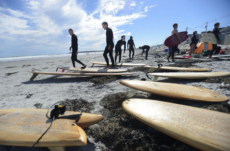 Surfers including Rand Budd, left, of West Creek, N.J., and Bob Paradis, second from left, of Saco look over wooden surfboards on the beach during the second annual Surf Re-Evolution festival at Long Sands Beach in York on Sunday.