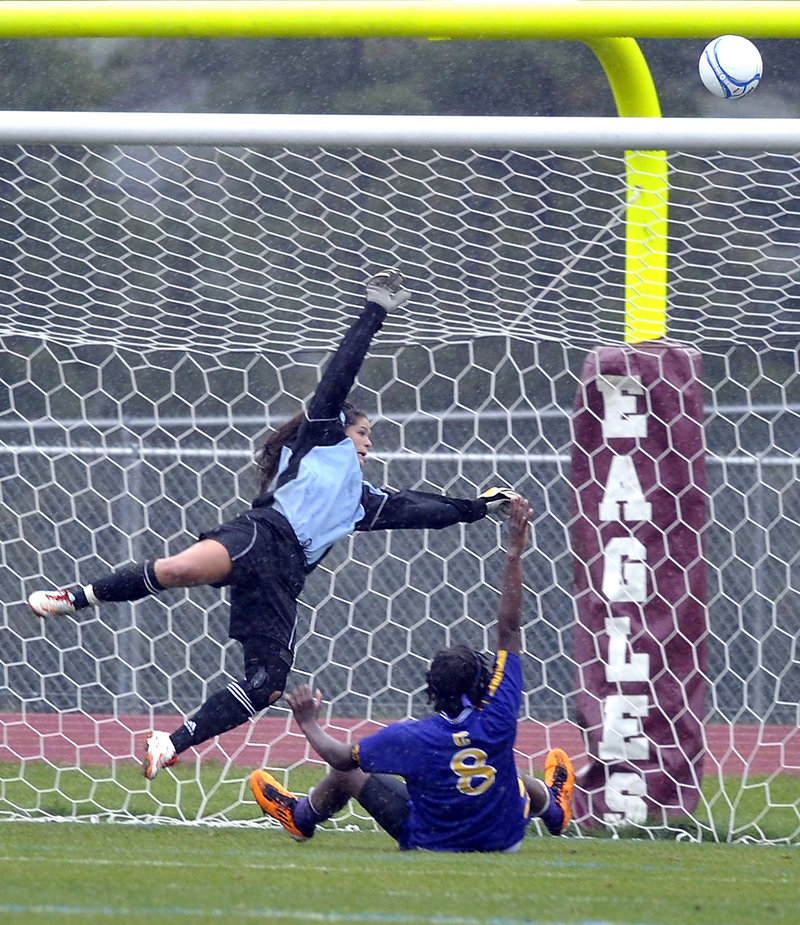 Windham goalkeeper Kate Kneeland, blocks a shot over the goal post as Sadie Lyons of Cheverus slides in Tuesday during Windham’s 3-1 girls’ soccer victory at home.