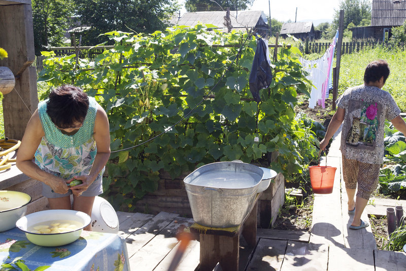 During summer months, the kitchen is moved outdoors. Here, Svetlana is peeling potatoes while her sister, Valya Zharavleva takes kitchen scraps to her compost pile at the edge of the garden.