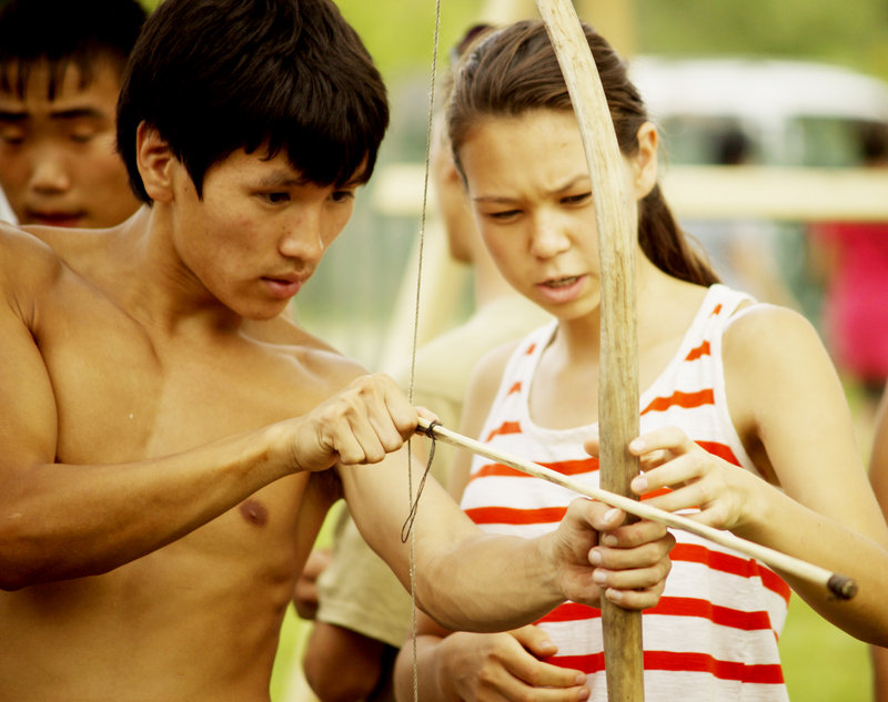 A village boy, Yura Kunchuga, teaches Ihila to use a bow and arrow during a competition at the summer festival.