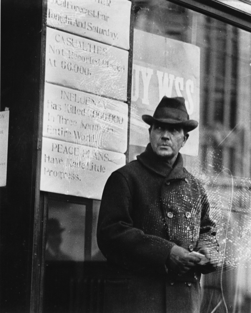 A man stands outside of the Press Herald/Telegram building during World War I. One of the signs behind him reads, "Influenza has killed 6,000,000 in three months in entire world." Credit: Gannett Collection, Maine Historical Society: