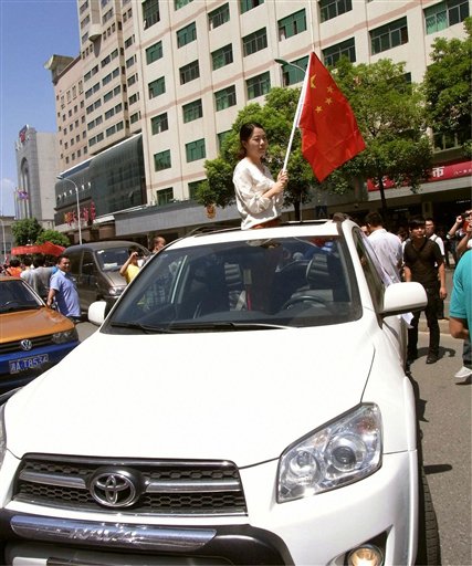 In this Sept. 15, 2012 photo, a woman holding a Chinese flag calls for protesters not to attack her Toyota car during the anti-Japan protest in Chongsha in China's Hunan Province. Toyota is shrugging off a sales plunge in China set off by a territorial dispute and says it is headed to a record year on the back of strong growth in the rest of Asia and the U.S. Toyota Motor Corp. Executive Vice President Yukitoshi Funo acknowledged Monday, Oct. 29 that achieving the company's target of 9.76 million vehicle sales this year will be harder because of the problems in China. Violent protests and a call to boycott Japanese goods erupted after Tokyo nationalized tiny islands that are controlled by Japan but claimed by Beijing. (AP Photo/Kyodo News) JAPAN OUT, MANDATORY CREDIT, NO LICENSING IN CHINA, FRANCE, HONG KONG, JAPAN AND SOUTH KOREA