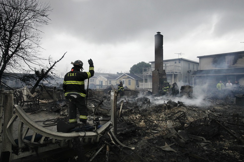 A fire fighter surveys the smoldering ruins of a house in the Breezy Point section of New York, Tuesday, Oct. 30, 2012. More than 50 homes were destroyed in a fire which swept through the oceanfront community during superstorm Sandy. (AP Photo/Mark Lennihan)