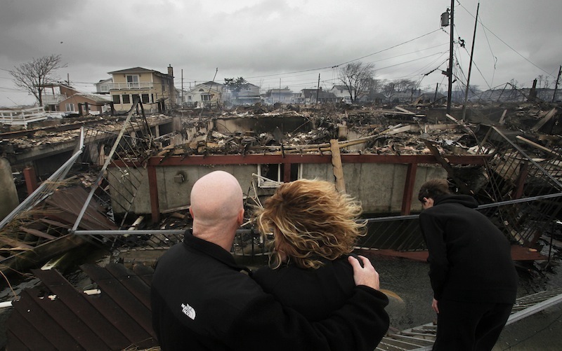 Robert Connolly, left, embraces his wife Laura as they survey the remains of the home owned by her parents that burned to the ground in the Breezy Point section of New York, Tuesday, Oct. 30, 2012. More than 50 homes were destroyed in the fire which swept through the oceanfront community during superstorm Sandy. At right is their son, Kyle. (AP Photo/Mark Lennihan)
