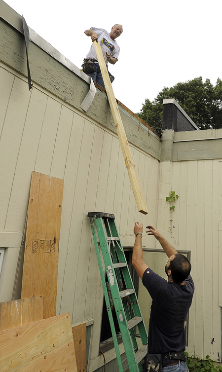 Bill Colby, left, top, of Colby Contractors in South Portland, receives a wood board from Aaron Gallagher, right, as the two work to seal the damaged roof of the Hall Elementary School before a storm arrives in this Tuesday, September 18, 2012 file photo. The school was damaged in an early-morning fire.