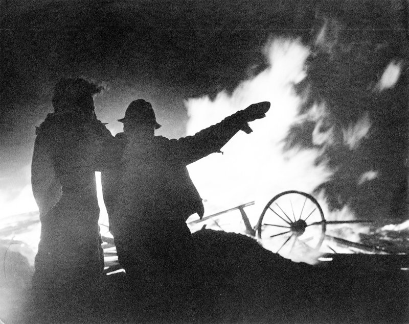 Firefighters are silhouetted against a plume of flames as they plan strategy during one of the 1947 fires.