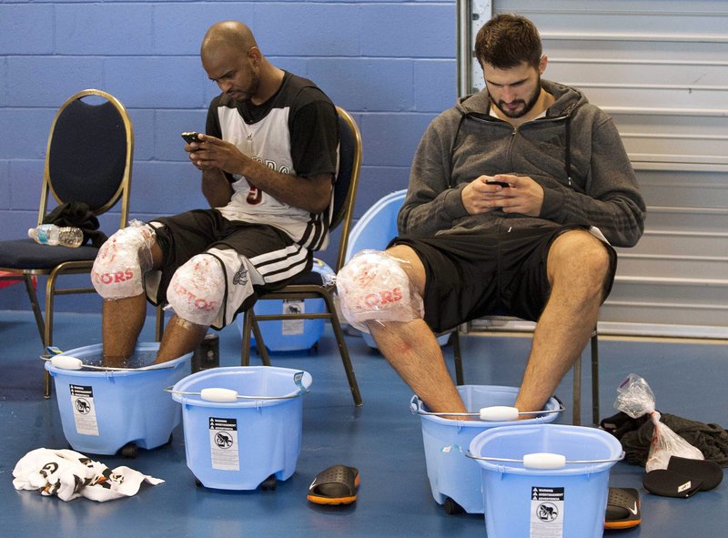 John Lucas III, left, and Linas Kleiza keep their feet on ice while using mobile devices Thursday during training camp for the Toronto Raptors in Halifax, Nova Scotia.