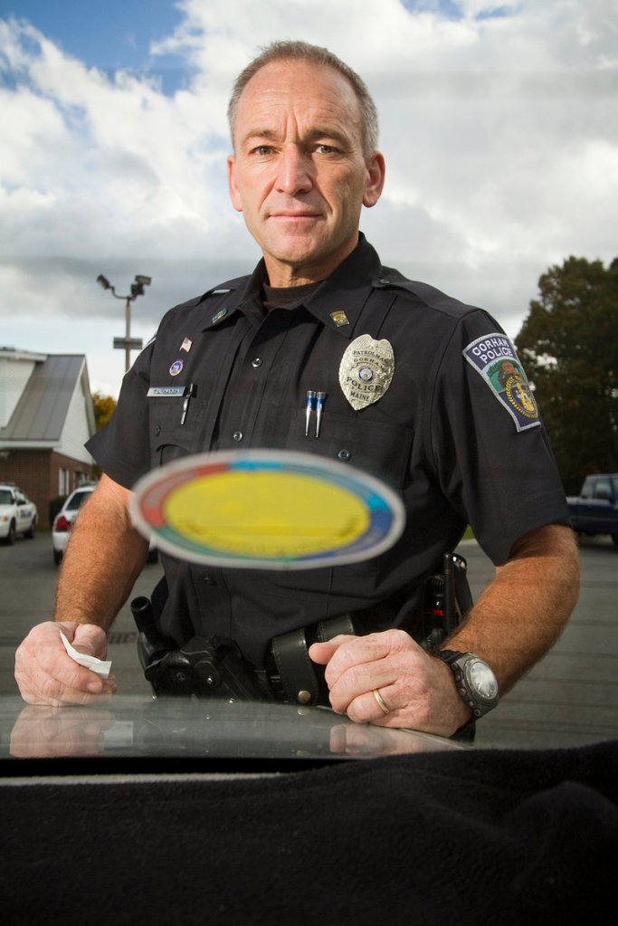 Gorham police Officer Ted Hatch stands outside a car’s rear window that has a Yellow Dot program sticker on Monday. The decal tells emergency responders that medical information can be found in the glove compartment.