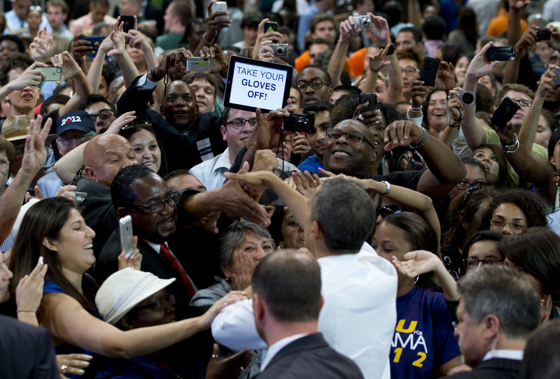 A person in the crowd holds up a sign that reads “TAKE YOUR GLOVES OFF” as President Obama shakes hands at a campaign event at the University of Miami on Thursday.