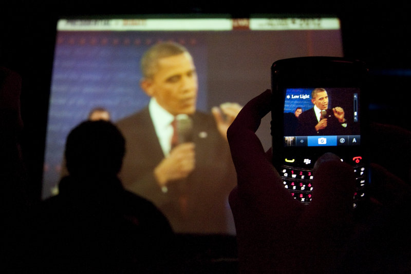 A spectator uses a phone to shoot a photo of a big-screen image of President Obama shown at Empire Dine and Dance in Portland.