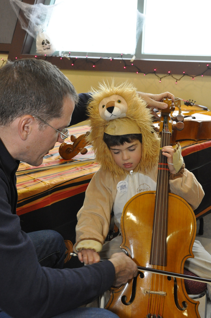 PSO music librarian Jon Poupore teaches a young lion about the cello in the “petting zoo.”
