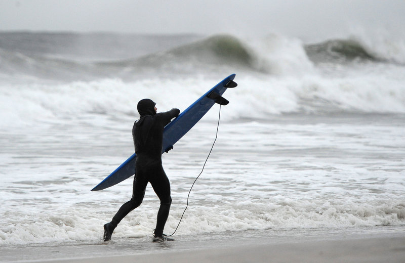 A surfer holds tight to his board against the strong winds and high surf of the Atlantic Ocean before the arrival of Hurricane Sandy on Sunday in Long Beach, N.Y.