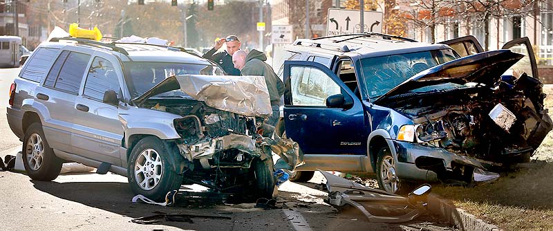 Police officers investigate a head-on collision on Marginal Way in Portland Sunday. The crash sent all 10 of the two vehicles’ occupants to hospitals with numerous injuries, police said.