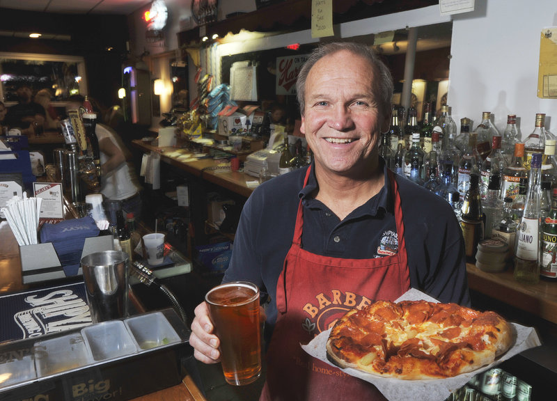 Howie Chadbourne, owner of Howie’s Pub in Portland’s East Deering neighborhood, offers up a draft beer and a pizza.