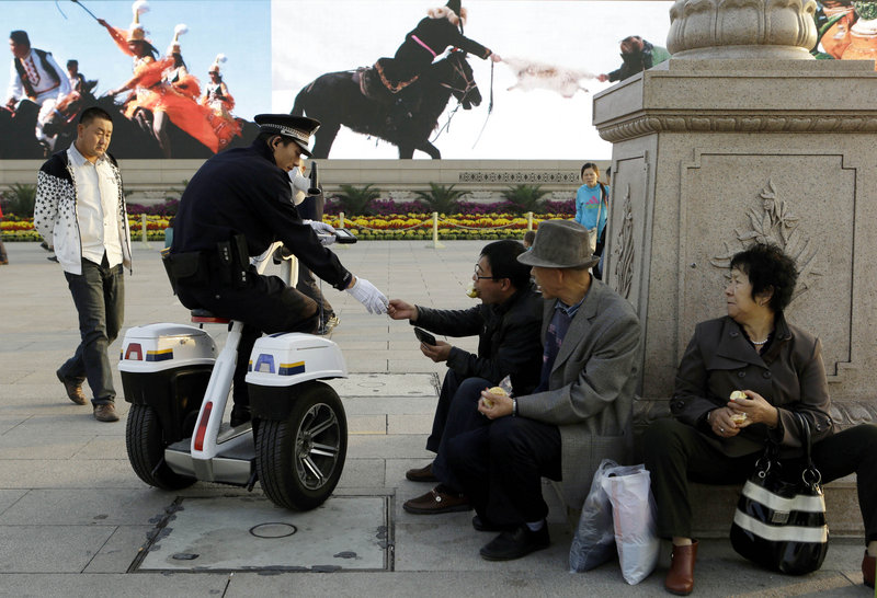 A Chinese police officer checks the identity of Chinese men resting Oct. 24 on Tiananmen Square in Beijing, near the site of the Chinese Communist Party’s 18th national Party Congress on Nov. 8. During the once-a-decade political transition, President Hu Jintao and most of the party leadership will begin to hand over power to younger colleagues.