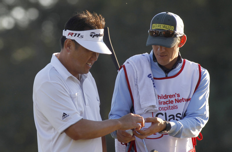 Charlie Wi, left, hands a ball to caddy Mark Urbanek, after finishing his first round at the Children’s Miracle Network Hospitals Classic at Lake Buena Vista, Fla., on Thursday.