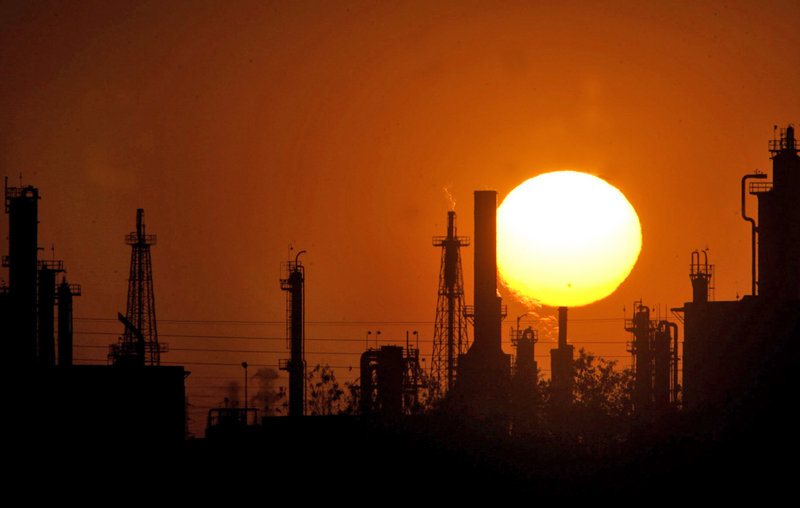The sun sets behind an oil refinery in Bakersfield, Calif. On Wednesday, the state is launching a cap-and-trade system meant to control emissions of heat-trapping gases, hoping the program provides a blueprint for other governments, says the California Air Resources Board.