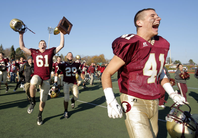 Jordan Matthews, left, can’t contain his excitement about getting a chance to hold the Gold Ball as Alex Rizeakos, center, Joshua Cyr, right, and the rest of the Thornton Academy football team celebrate their victory Saturday over Lawrence in the Class A state championship game.