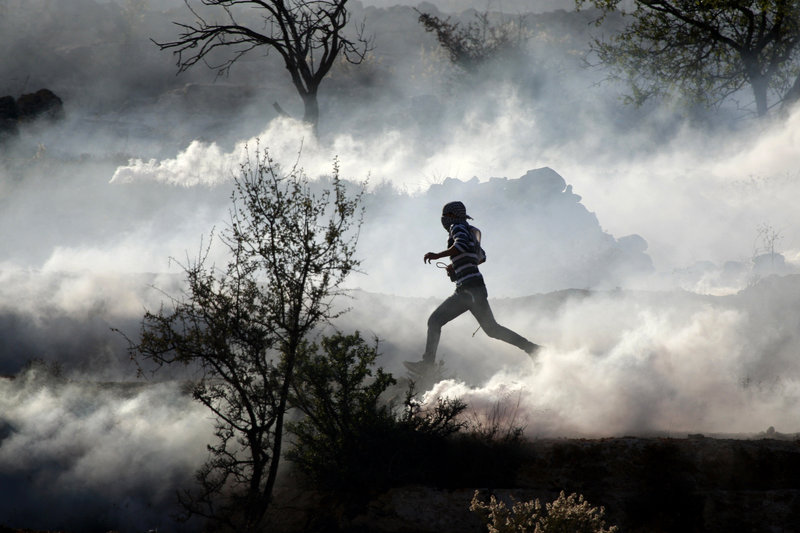 A Palestinian demonstrator runs through tear gas Thursday during clashes against Israel’s operations in the Gaza Strip outside Ofer, an Israeli military prison near Ramallah.
