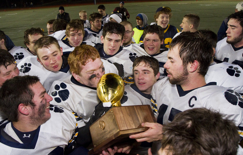 Jordan Whitney, the Mt. Blue quarterback, right, holds the Gold Ball for a teammate to kiss Saturday night after the Cougars beat Marshwood to win the Class B title.