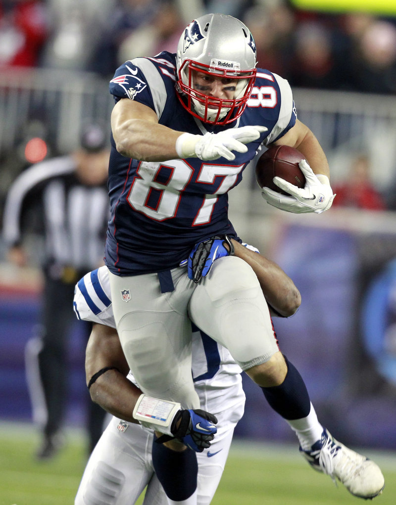 Rob Gronkowski gains extra yardage while dragging an Indianapolis defender during first-half action of Sunday’s rout of the Colts in Foxborough, Mass. But Gronkowski’s stellar day was ruined by a broken arm that may sideline him for the rest of the regular season.
