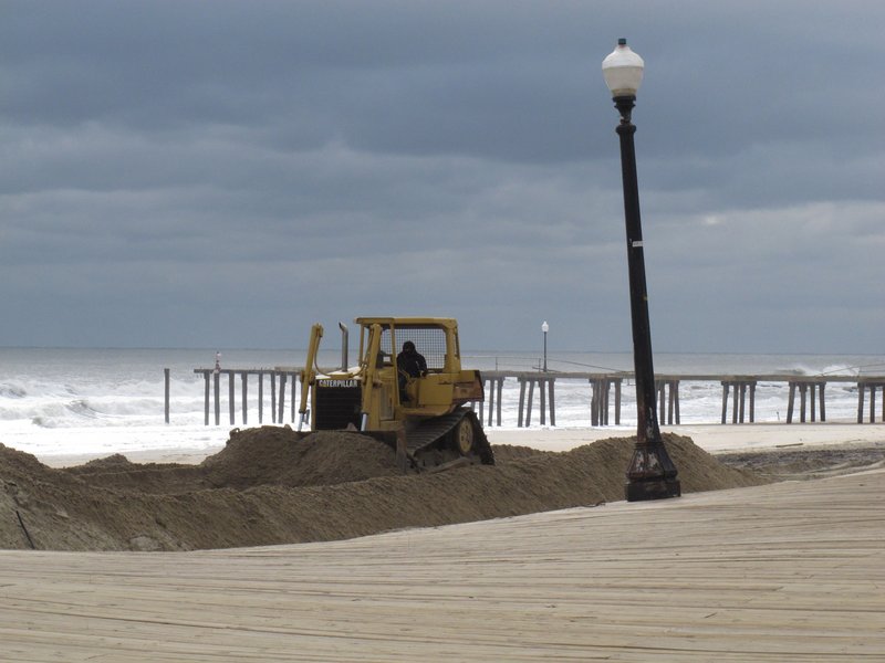 A bulldozer pushes piles of sand on the Ocean Grove, N.J., beach in front of its storm-buckled boardwalk and damaged fishing pier last week.