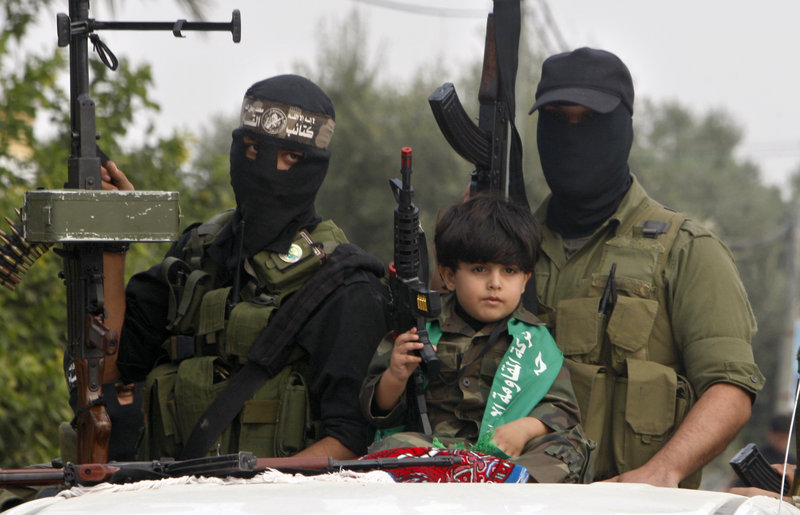 A Palestinian boy and militants of the Izzedine Al-Qassam Brigades attend funerals in central Gaza Strip of five Hamas militants killed in an Israeli airstrike.