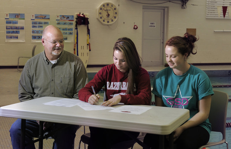 Sarah Easterling, center, singing a letter of intent to attend the University of Arkansas Monday, is flanked by her father, Jeff, and her twin sister, Sidney, who also swims for Greely.
