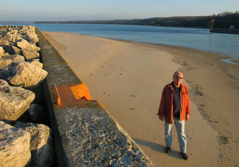 Jim Simons, who runs a rod and reel repair business, strolls on a sandbar by the channel leading to Lake Michigan at Onekama, Mich. The bar normally would be submerged, but low water levels have exposed the the bottom in many areas.