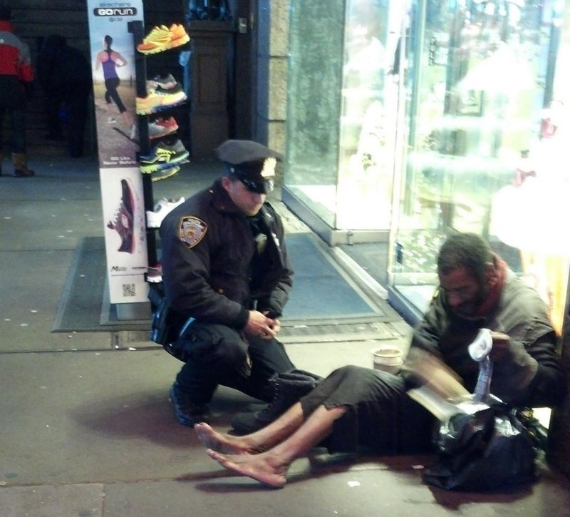 Photo provided by Jennifer Foster of Florence, Ariz., shows New York City Police Officer Larry DePrimo presenting socks and boots to a barefoot homeless man in New York’s Time Square on Nov. 14.