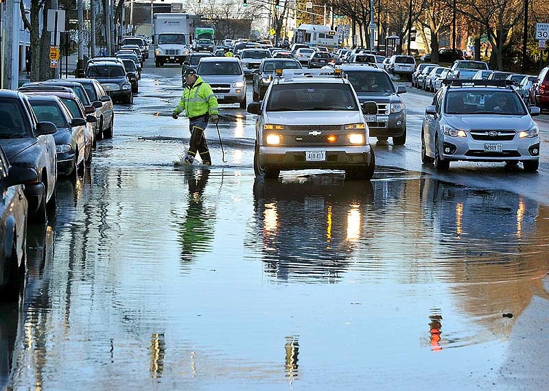 Portland Public Service worker Carl Leonard wades through the water as a water main break on Park Avenue near Mellen Street slowed traffic during morning rush hour on Thursday.