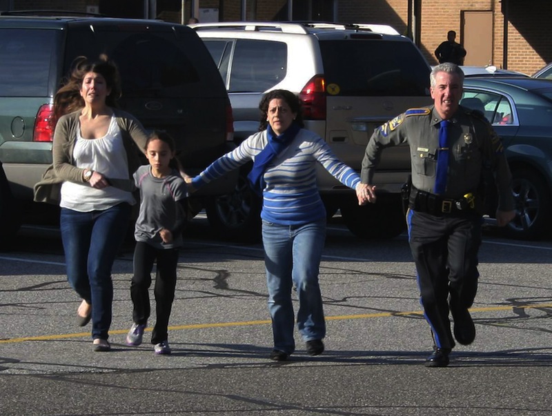 In this photo provided by the Newtown Bee, a police officer leads two women and a child from Sandy Hook Elementary School in Newtown, Conn., where a gunman opened fire, killing 26 people, including 20 children, Friday, Dec. 14, 2012. (AP Photo/Newtown Bee, Shannon Hicks)