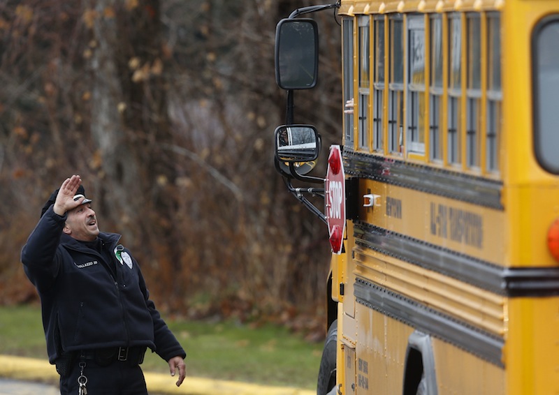 Easton police officer J. Sollazzo waves to returning children as their bus pulls into Hawley School, Tuesday, Dec. 18, 2012, in Newtown, Conn. Classes resume Tuesday for Newtown schools except those at Sandy Hook. Buses ferrying students to schools were festooned with large green and white ribbons on the front grills, the colors of Sandy Hook. At Newtown High School, students in sweatshirts and jackets, many wearing headphones, betrayed mixed emotions. Adam Lanza walked into Sandy Hook Elementary School in Newtown, Friday and opened fire, killing 26 people, including 20 children, before killing himself.(AP Photo/Jason DeCrow)
