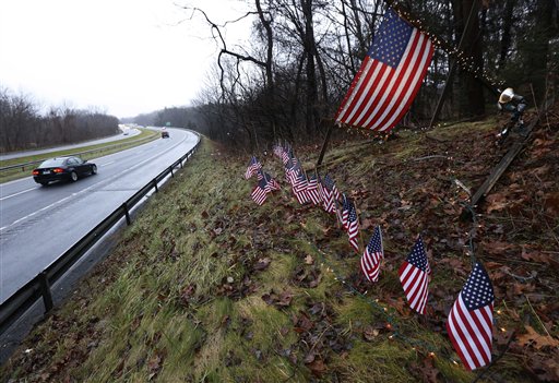 A makeshift memorial of 27 small and one large American flag stands by the side of Highway 84 near the Newtown, Conn., town line on Monday.
