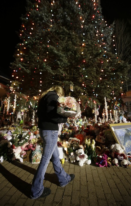 In this Thursday, Dec. 20, 2012 file photo, a woman with flowers walks past a Christmas tree which has become a memorial to the Newtown shooting victims in Newtown, Conn. In the wake of the shooting, the grieving town is trying to find meaning in Christmas. (AP Photo/Seth Wenig)