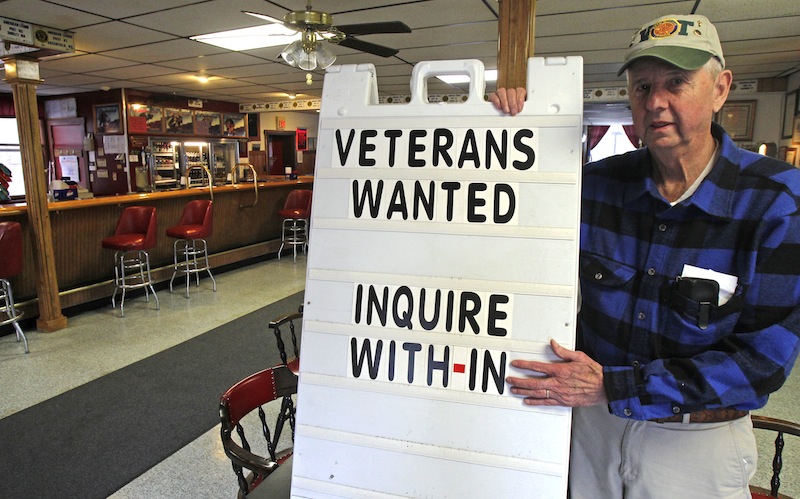 In this Wednesday, Dec. 19, 2012, Legion Post 3 Commander Dick Harlow poses with a sign in Montpelier, Vt. The American Legion post in Vermont’s capital city has a simple method to help attract new members: A sign in the Main Street doorway says “members wanted.” They still get new members, sometimes veterans of Iraq and Afghanistan, but few of them are young, most are in their 40s or even older. (AP Photo/Toby Talbot)