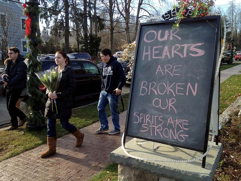 Jessica Henderson, 19, walks past a sign with a bouquet of flowers to lay at a memorial at The Sandy Hook School in Newtown, Conn., on Saturday.