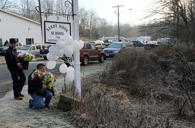A couple of volunteer firefighters place flowers at a makeshift memorial at a sign for the Sandy Hook Elementary school on Satuday.