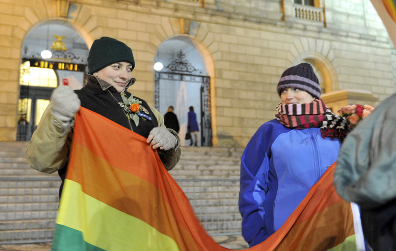 Amber Hardy of Portland and Amanda Poulin of Cape Elizabeth unfurl a gay pride flag in front of Portland City Hall on Friday before the first same-sex marriages were performed.