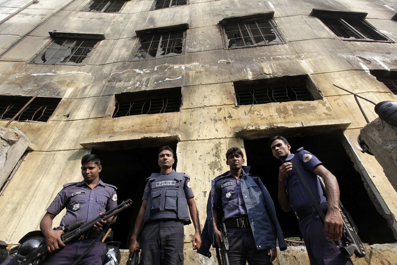 Police officers gather in front of a burned-out garment factory in Bangladesh. A fire last Saturday raced through the building, killing 112 workers and putting new focus on the working conditions for many overseas workers.