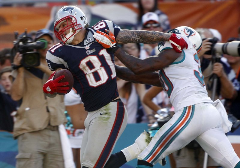 Patriots tight end Aaron Hernandez tries to stiff-arm Dolphins safety Chris Clemons during Sunday’s game at Miami, won by the Patriots, who are again bound for the postseason.