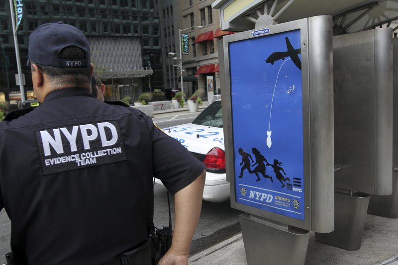 New York City police officers wait to remove a fake NYPD 'public service' ad in Lower Manhattan. The posters, allegedly posted by former Maine student Essam Attia, depict the police force as a drone-deploying Big Brother.