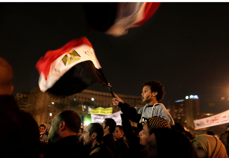A young Egyptian boy waves a national flag from his mother’s shoulders as thousands of protesters gather and chant slogans in Tahrir Square in Cairo on Tuesday.