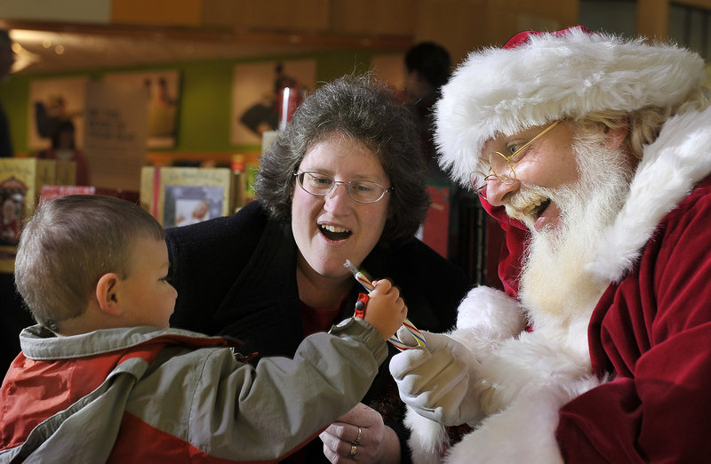 The roles are reversed as 2-year-old William Burke of Gray hands a candy cane to Santa as grandmother Elizabeth Burke watches at the Maine Mall in South Portland on Friday. This Santa replaces a previous one at the mall who drew some complaints.