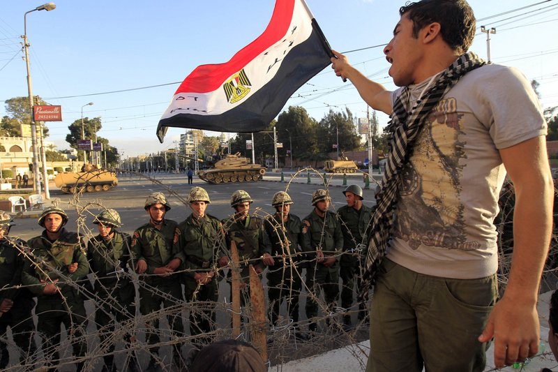 A protester waves an Egyptian flag in front of Republican Guard soldiers standing behind a barricade and guarding the presidential palace in Cairo on Friday.